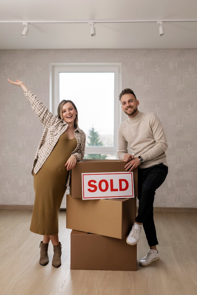 Excited pregnant couple celebrating their new home purchase with sold sign.